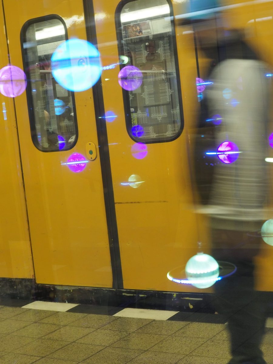 Einfahrende U-Bahn am Alt-Tempelhof, gespiegelt in der Glasscheibe mit leuchtenden Planeten